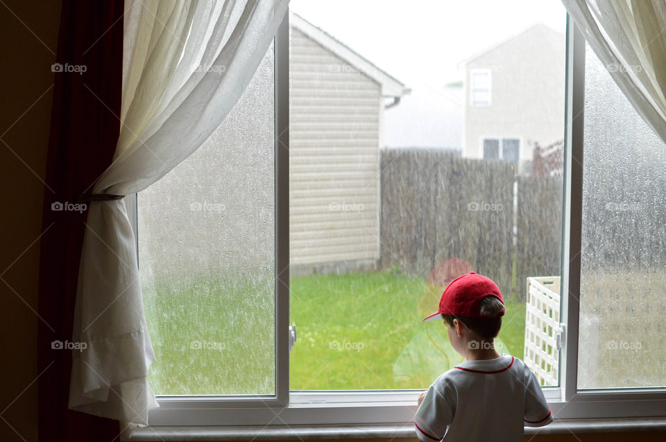 Young toddler boy looking out of a large window of a home on a rainy day