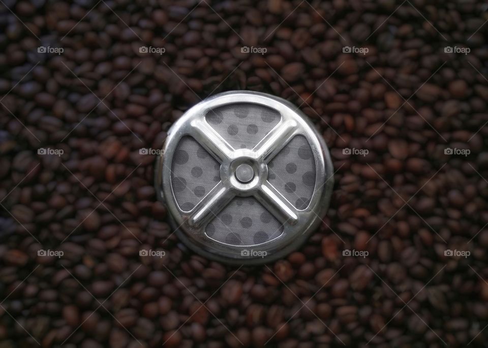 French press coffee maker strainer on a bed of whole coffee beans from above close up