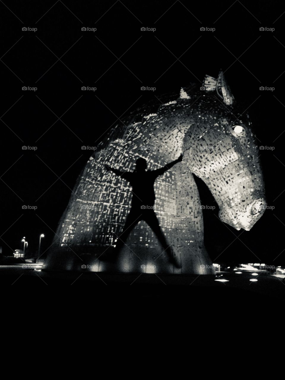 B&W photo of my son doing a star jump against a lit up background of one of the Kelpies ... 