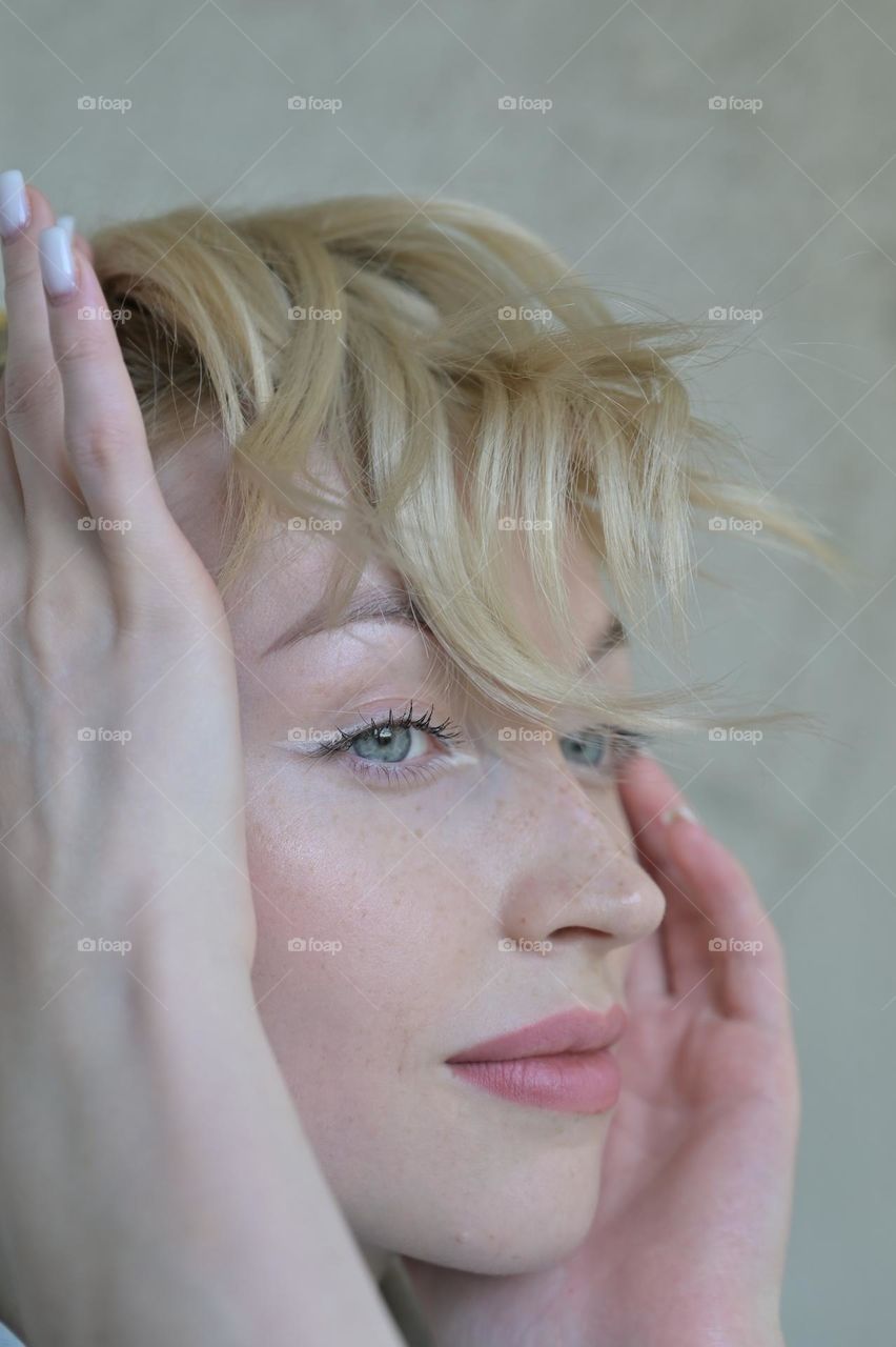 Portrait of a cute girl with blond hair with a beautiful look with her hands near her head