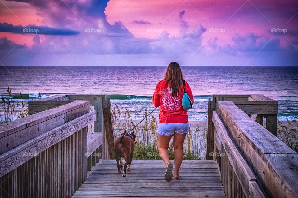 A woman and her dog heading out to enjoy the beach under a beautiful purple early morning sky. Emerald Isle, North Carolina. 