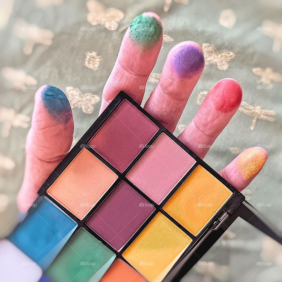 Woman’s hand holding eye shadow palette, bright eye shadow colors on woman’s fingertips, holding onto makeup, beauty contest, brightly colored eye shadows