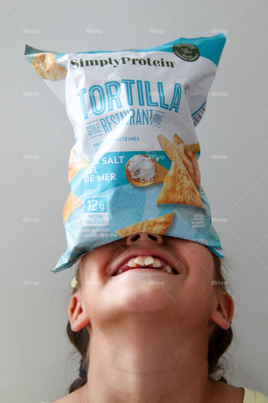 Cute happy girl balancing bag of chips on her head