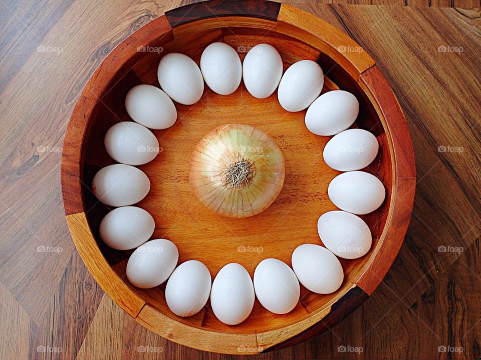 Eggs in a circle around an onion in a wood bowl 