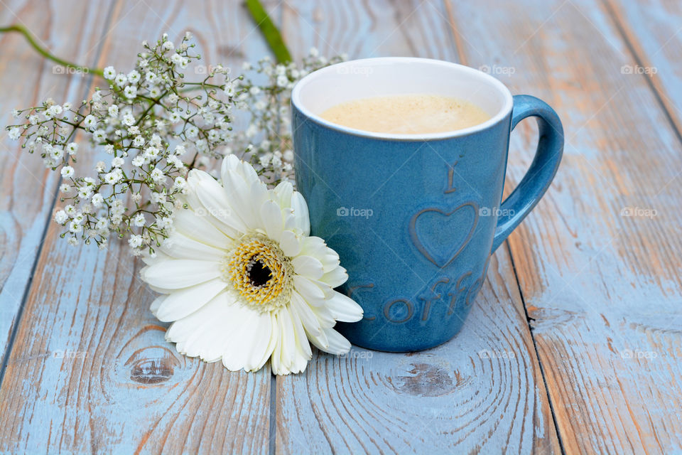 blue cup of coffee on a wooden table background with a white gerbera daisy flower