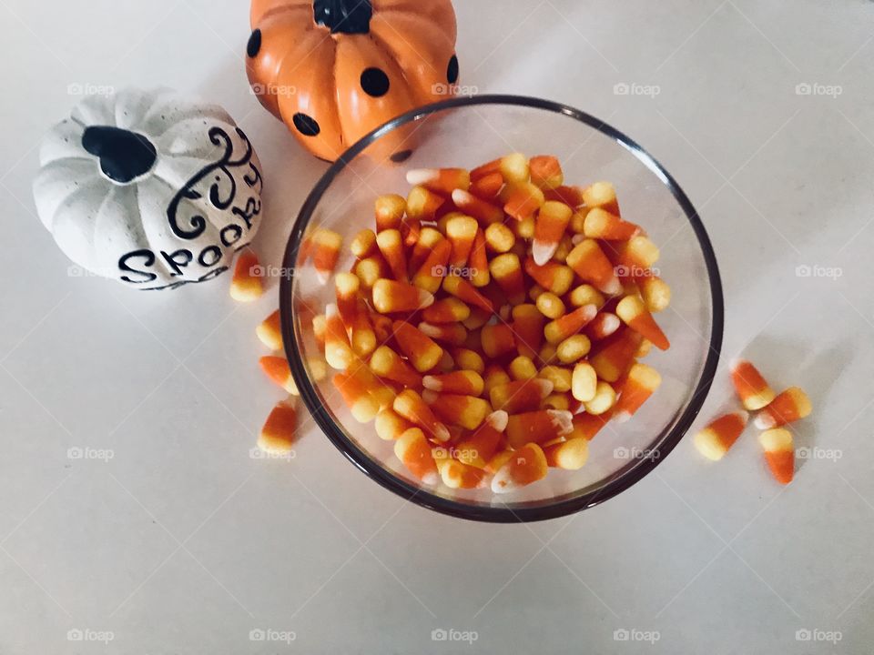 A delicious big bowl of candy corn candies surrounded by mini pumpkins, getting ready for Halloween night. 