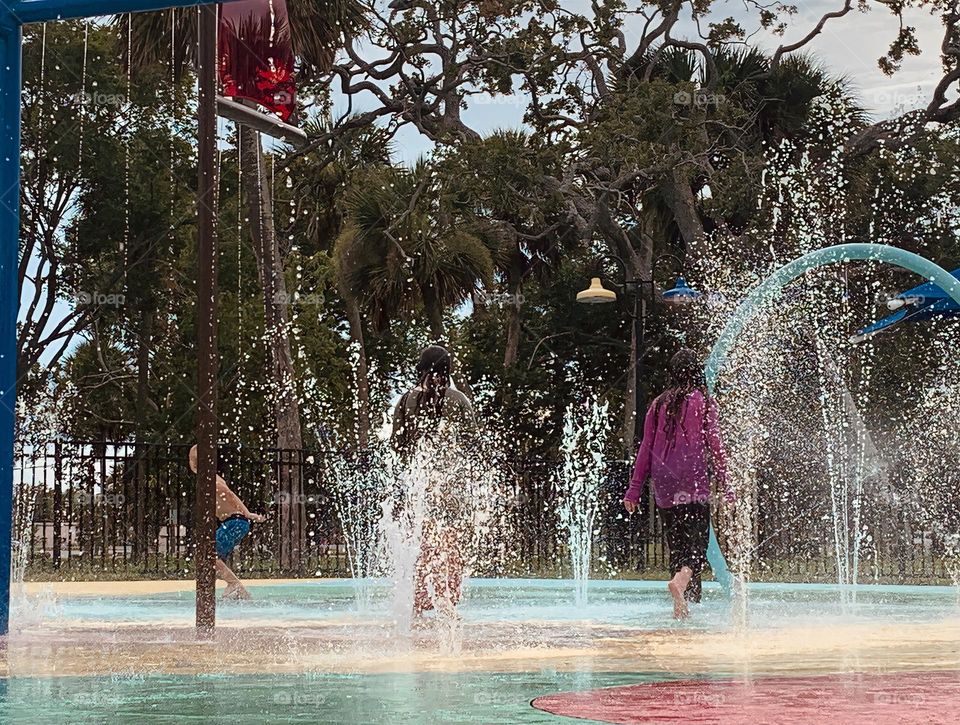 Children having lots of fun in the water at the colorful kids splash pad at the city park for children during a really warm day in Florida.