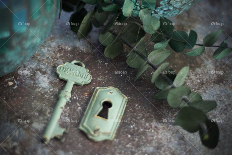 Light teal, metal vintage key with embossed word, “Dreams,” and keyhole on concrete surface 