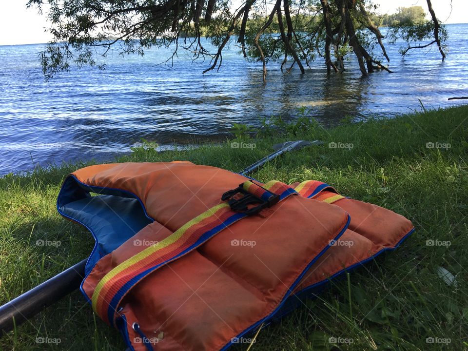 Retro Orange life jacket on shore with paddle overlooking water with trees conceptual healthy active lifestyle and safety background 