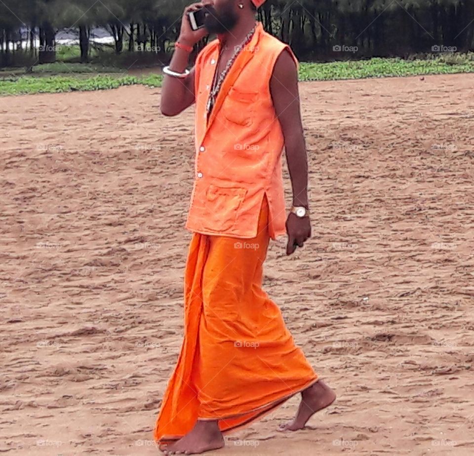 modernity in holy man of south Asia taking a walk on the beach