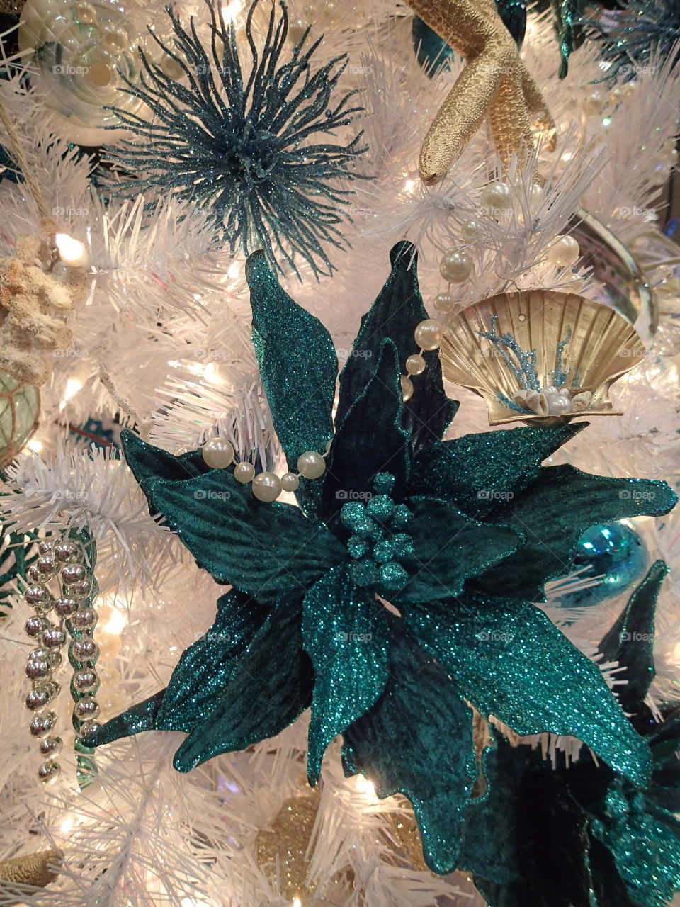 A glittering blue star hung on a white Christmas tree. 