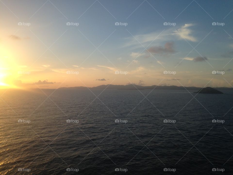 Sunset at sea with mountainous landscapes visible on the horizon and wispy clouds above