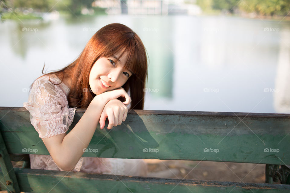 Cute young girl smiling on the chair in the park 