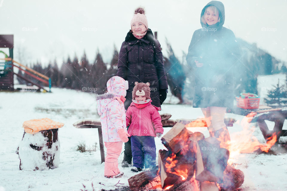 Family spending time together outdoors in the winter. Parents with children gathered around the campfire preparing marshmallows and snacks to toasting over the campfire using wooden sticks