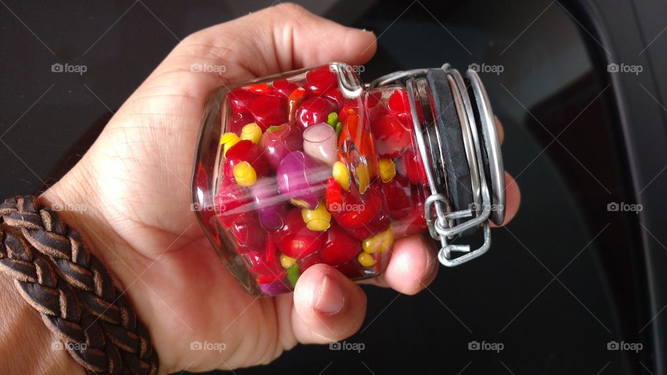 Mão com um frasco, vidro com pimentas coloridas.