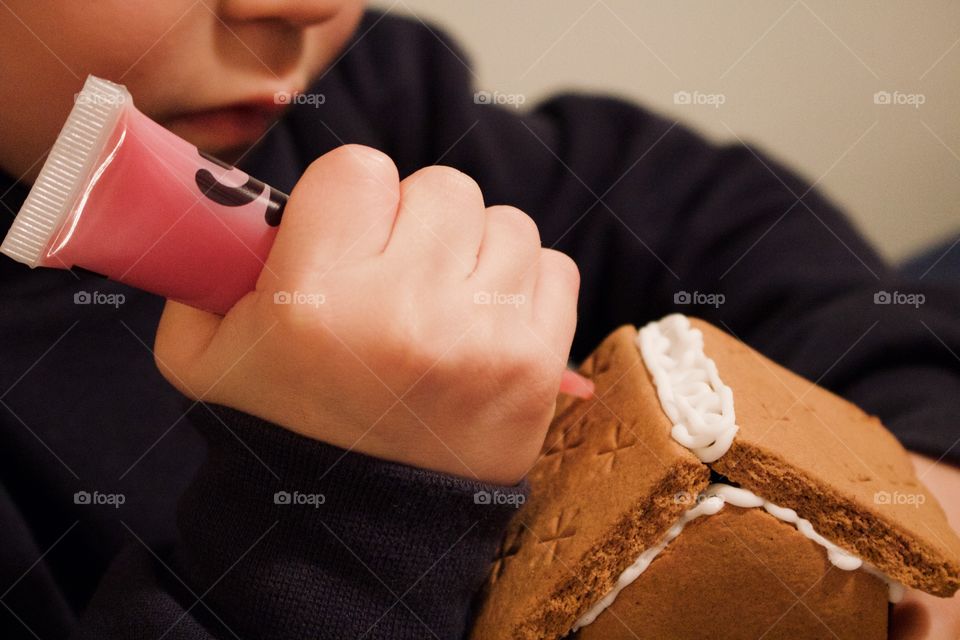 Little boy decorating a mini gingerbread house 