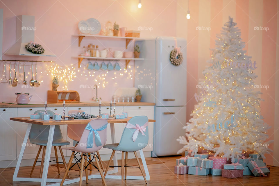 Festive winter cozy kitchen interior with garlands, decorations and gifts.  Christmas dinner at the decorated table.