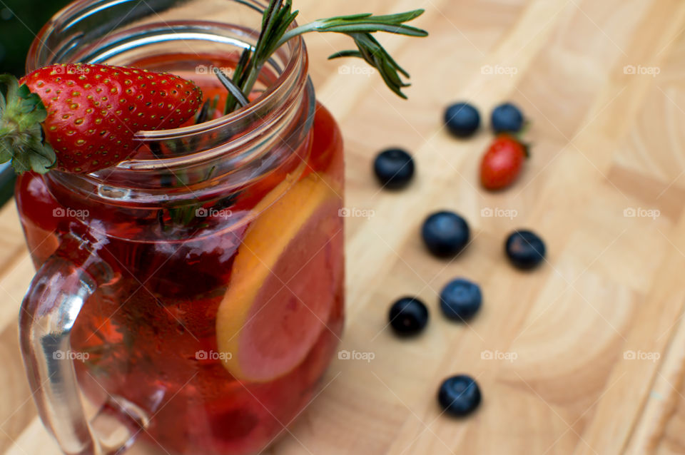 Elevated view of beautiful fresh berry flavored water in glass jar on wood with organic strawberry, blueberry, Rosemary and citrus sliced lemon lime for a homemade variation of gourmet berry lemonade