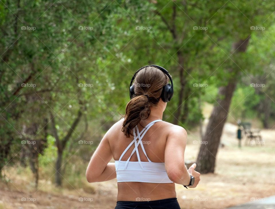 Rear view of female with headphones running in park during summer