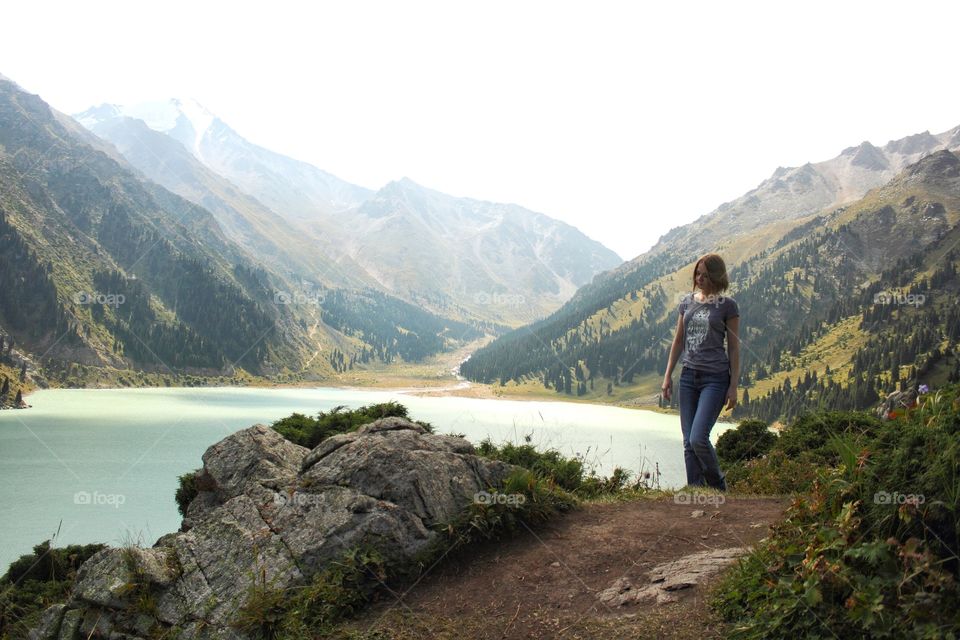 A girl climbs a path near a mountain lake