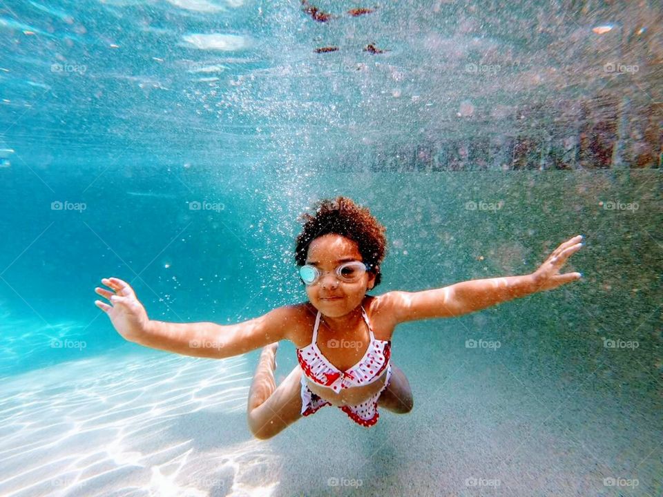 Child swimming underwater with goggles on in the pool.