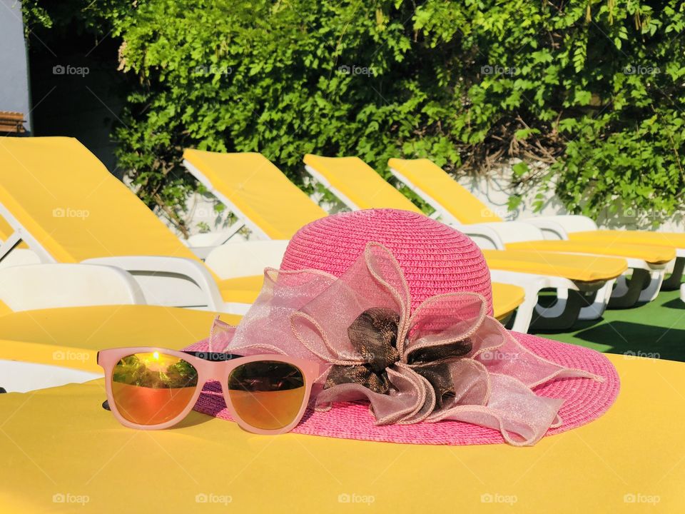 Pink sunglasses and a hat placed on a yellow sunbed with many yellow sunbeds in the background