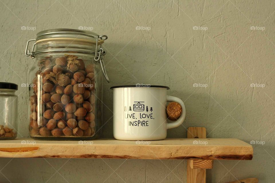 Wooden shelf with glass jars with peanuts and hazelnuts and a tin mug in the kitchen