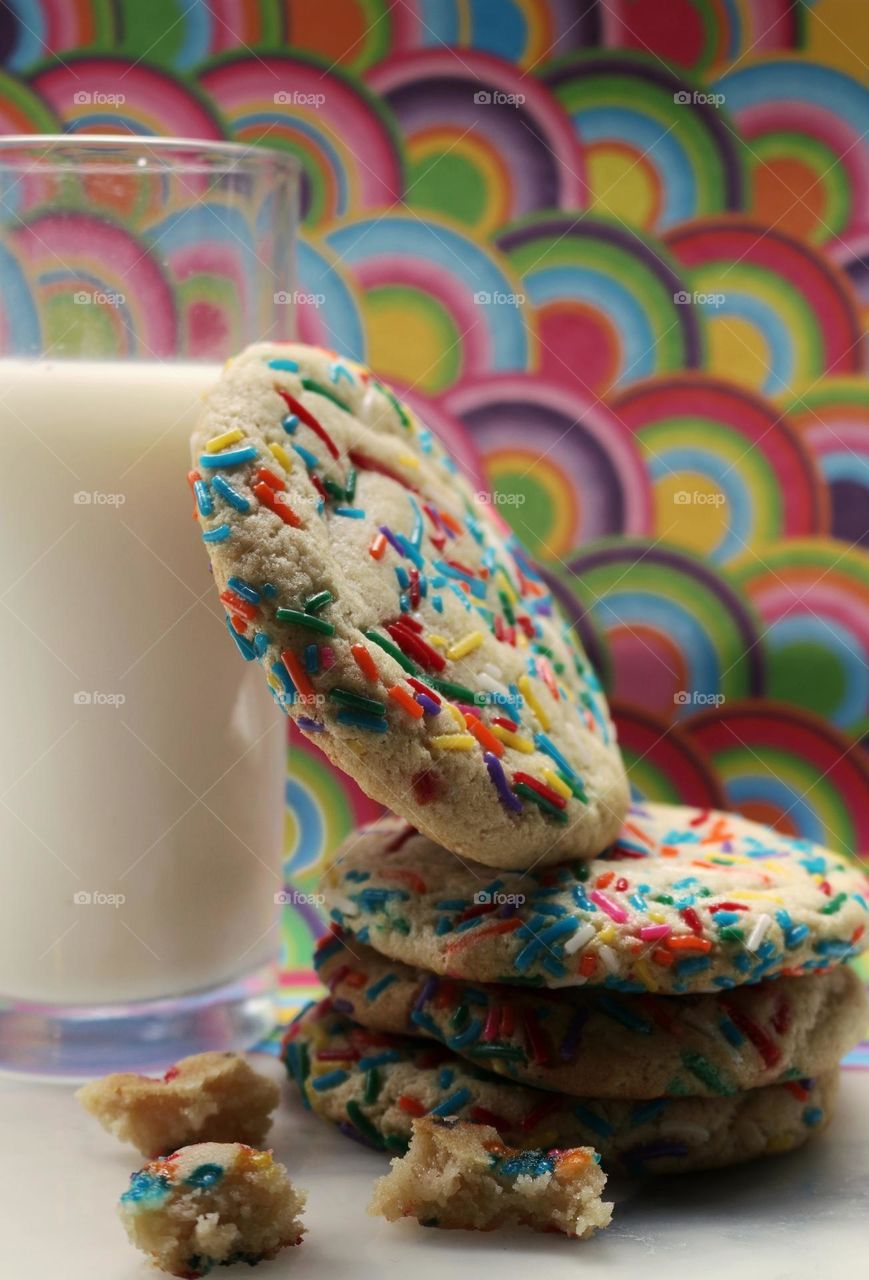 Rainbow sugar cookies alongside a glass of milk.