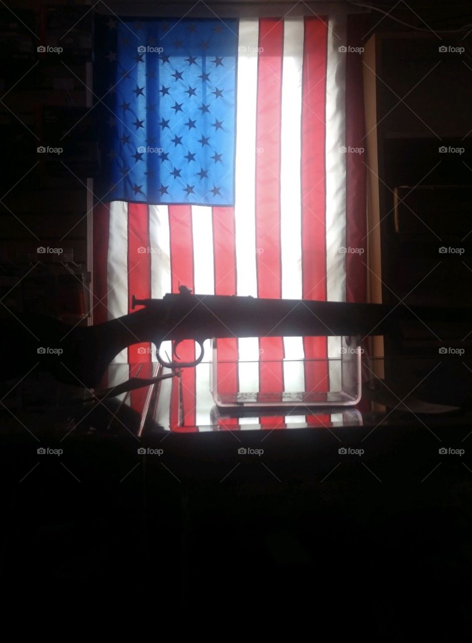 American Flag in a window with a firearm silhouette in the foreground 