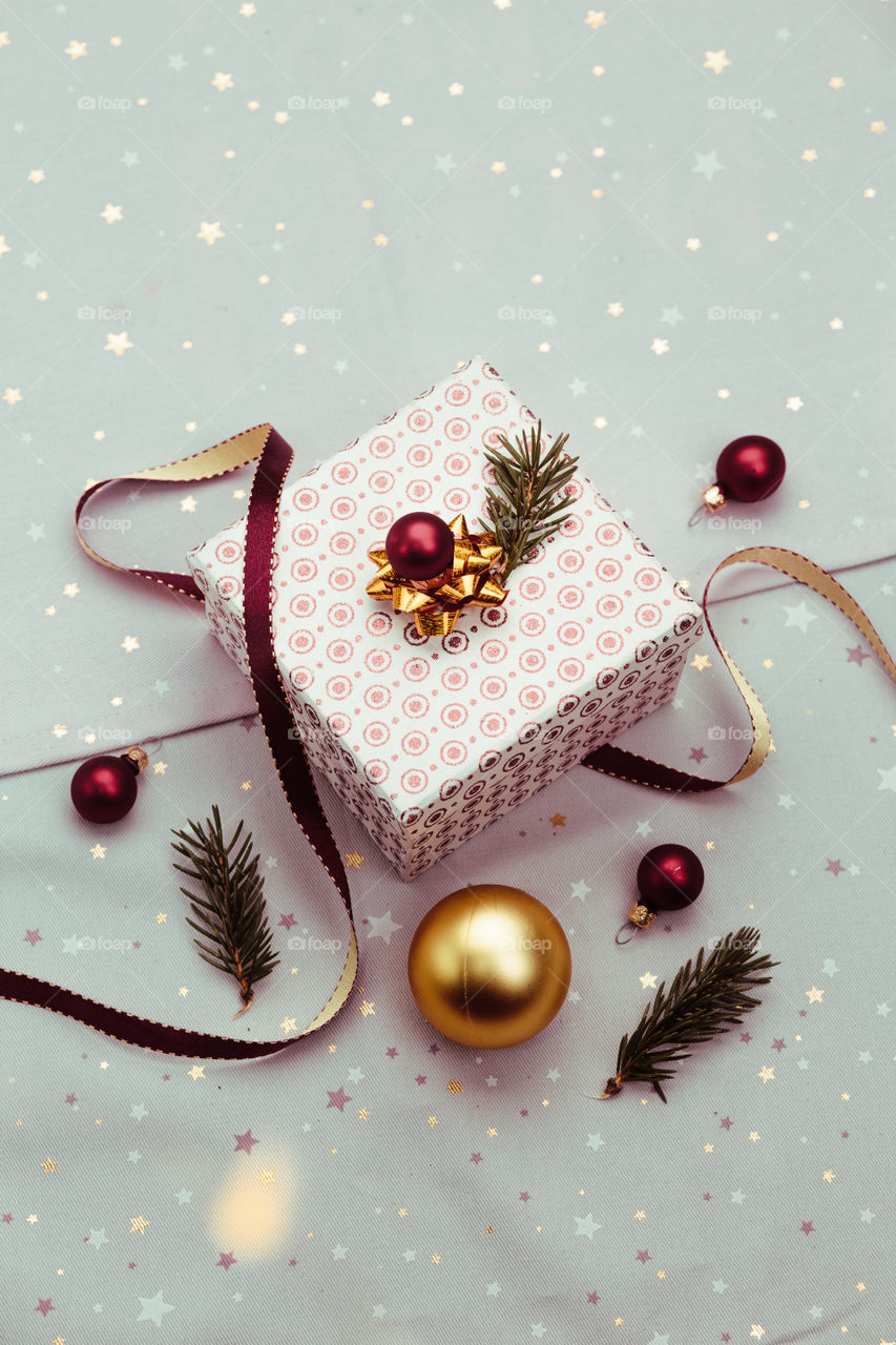 Wrapping Christmas gift into box. Decorating using red ribbon, red Christmas balls and pine twigs. Blurred Christmas lights. Flat top-down composition. Figure of angel made of earthen with love inscription as Christmas decoration