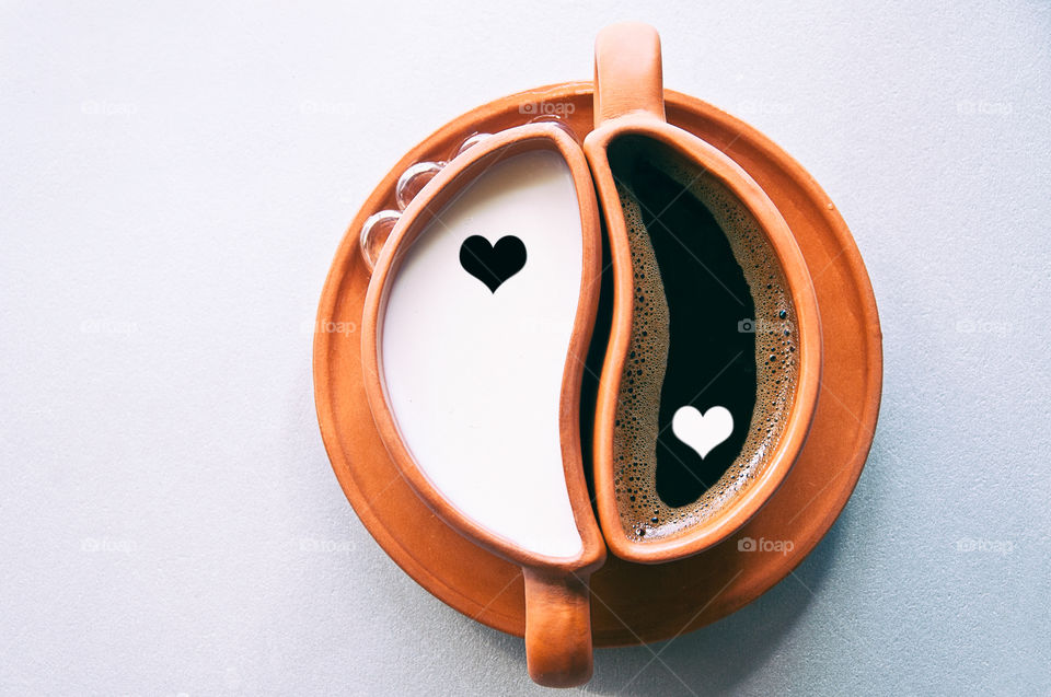 a pare of ying yang cups with coffee and milk and with heart patterns