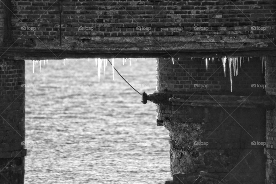 Black and white photo of icicles hanging from an old brick bridge on the North Sea