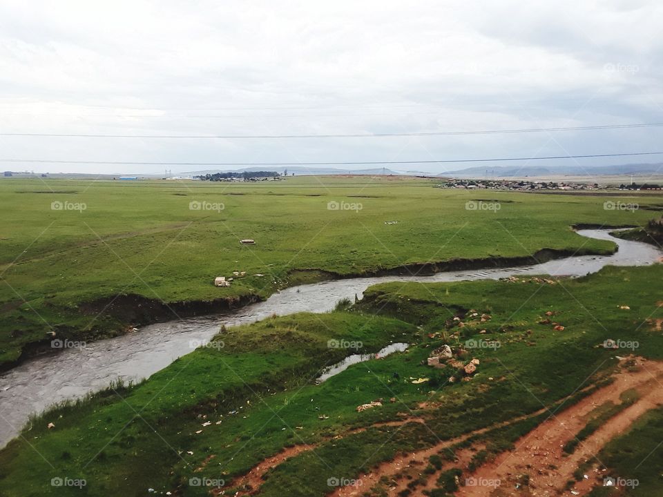 A stream flows through the grassland with cloudy skies at summertime.
