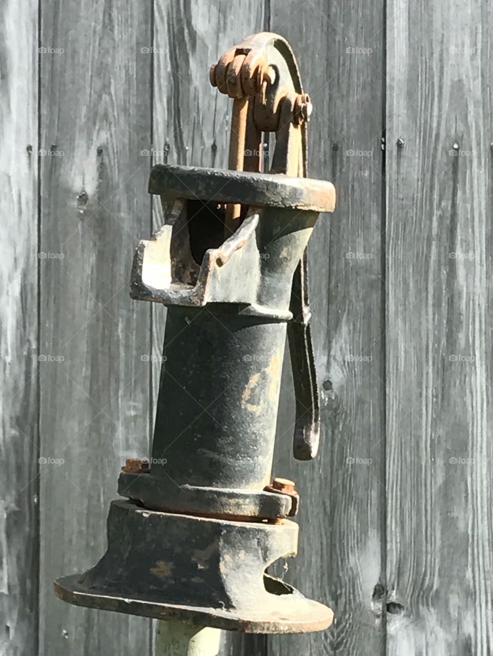 Closeup of an old style water pump with an old weathered wood sided shed in the background.