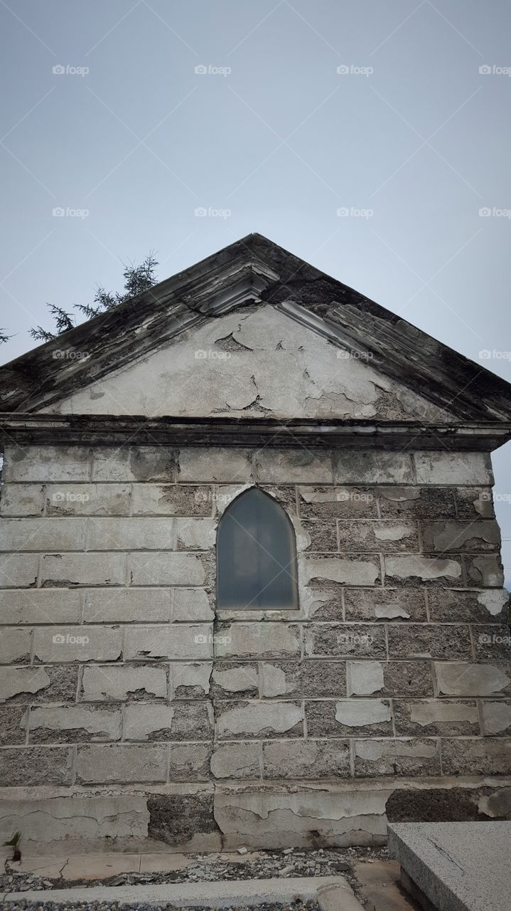 This small decaying building is the back of a family crypt. its earliest date was in the late 1800s. Taken on a cold rainy day. it seems every storm takes peels away a little from the crypt.