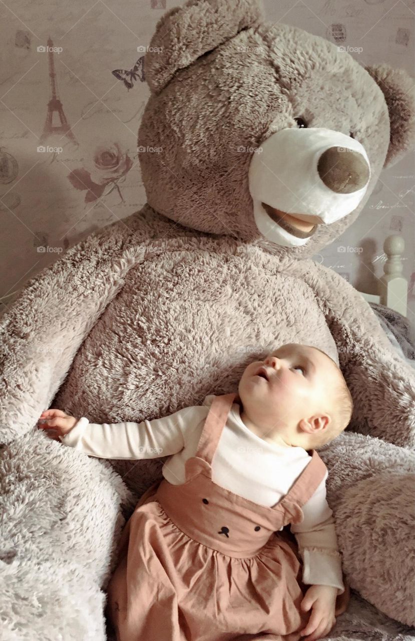 Young child looking surprised at her giant teddy bear 