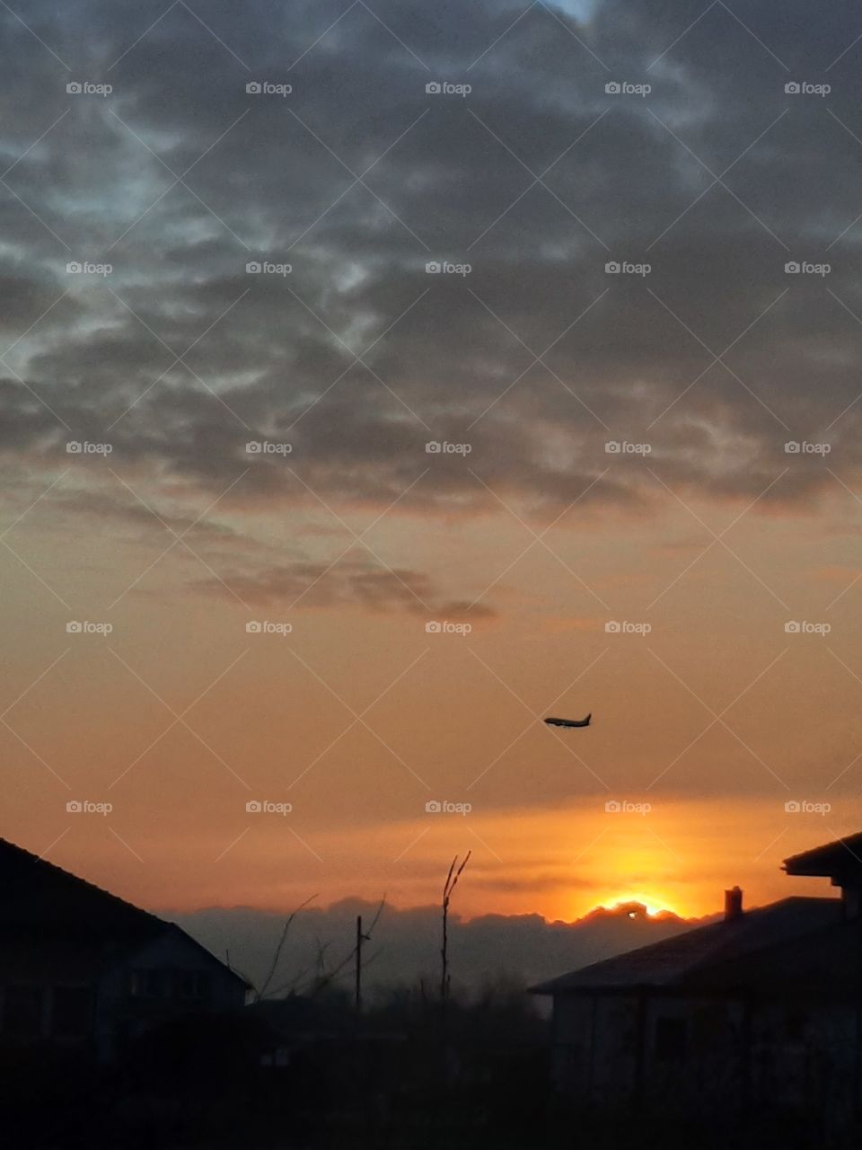 rising sun illuminating an aeroplane, orange sky and dark clouds