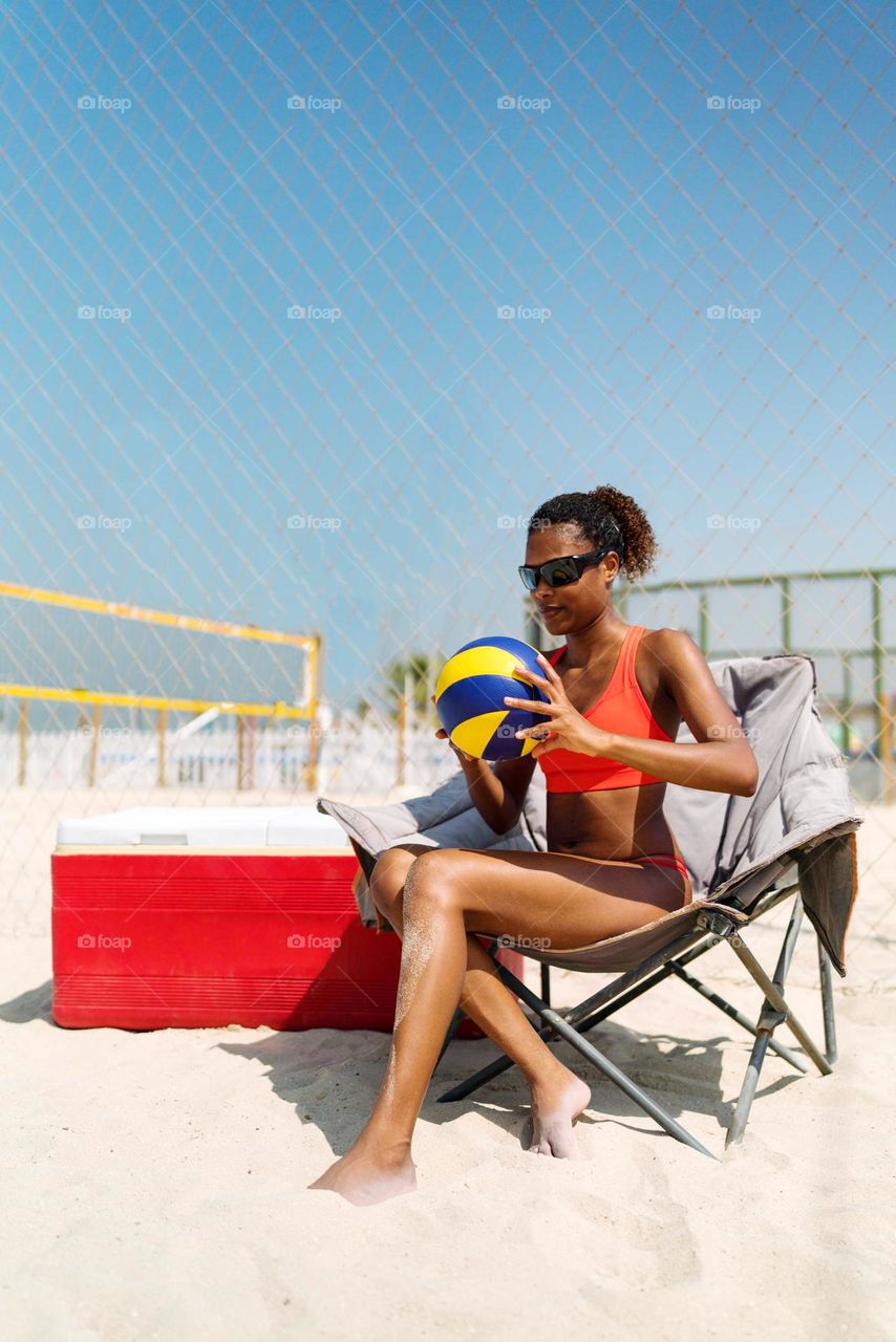 Beautiful black woman with Afro hair sitting holding a volleyball at the beach