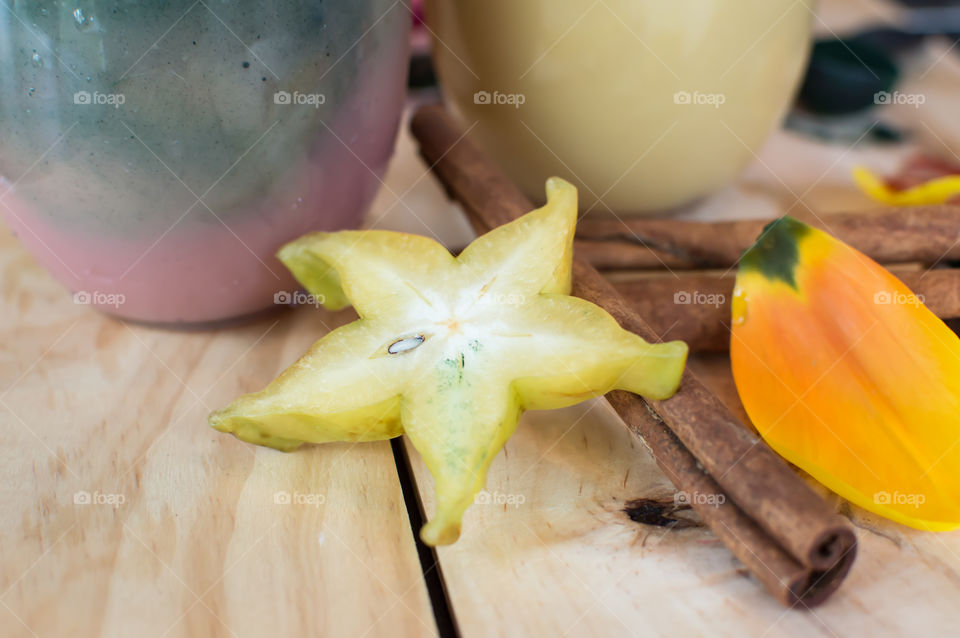 Low angle view of colorful fresh fruit smoothies with carambola fruit - star fruit and cinnamon stick ingredients on wood table in pastel Colors 