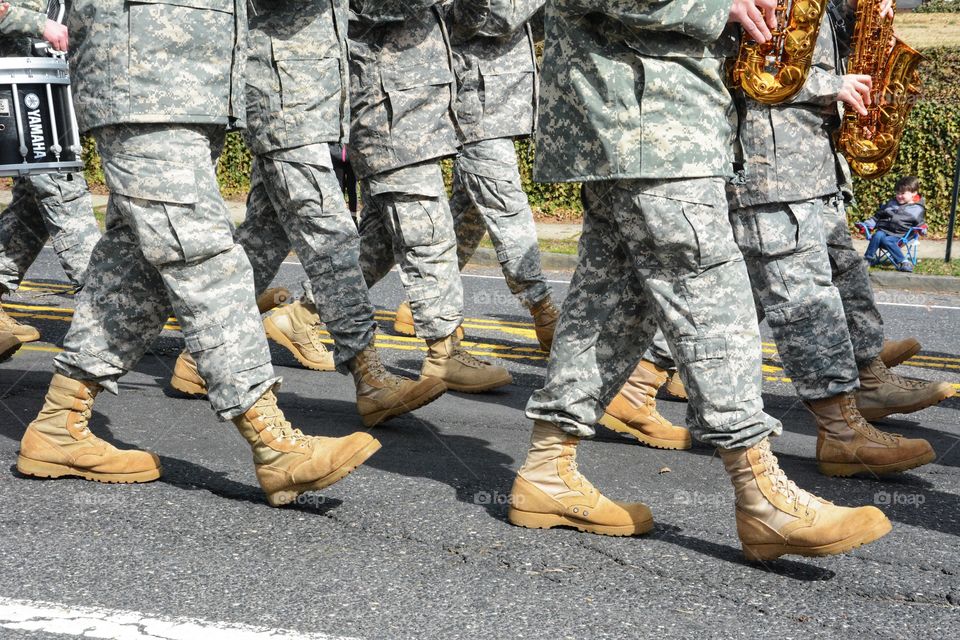 legs of army men/woman in camouflage and boots are seen marching in a parade