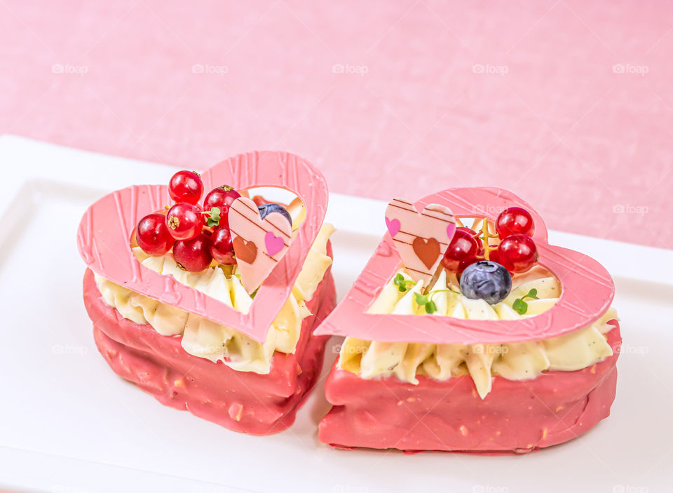 Heart shaped cakes filled with cream and berries on the white plate on the table.