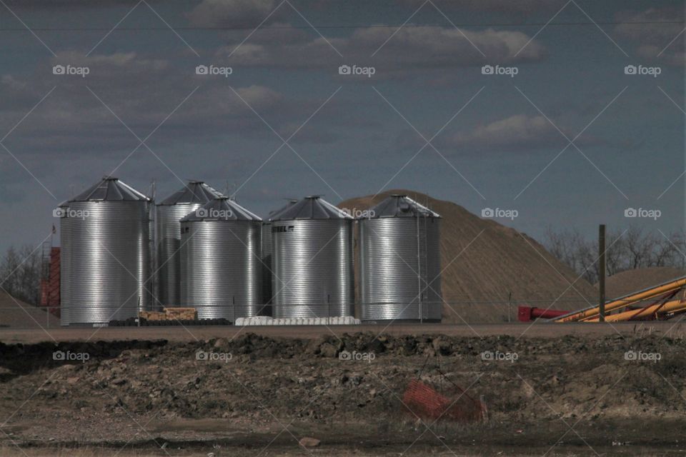 grain silos steel with mounds of dirt with blue sky and clouds