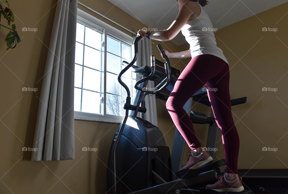 Young woman exercising on an elliptical machine in front of a window in the morning