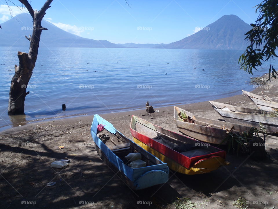 Cayucos and volcanoes. Boats native to Lake Atitlan, Guatemala, are called cayucos. Here they are lined up on the beach with 2 volcanoes across the lake.