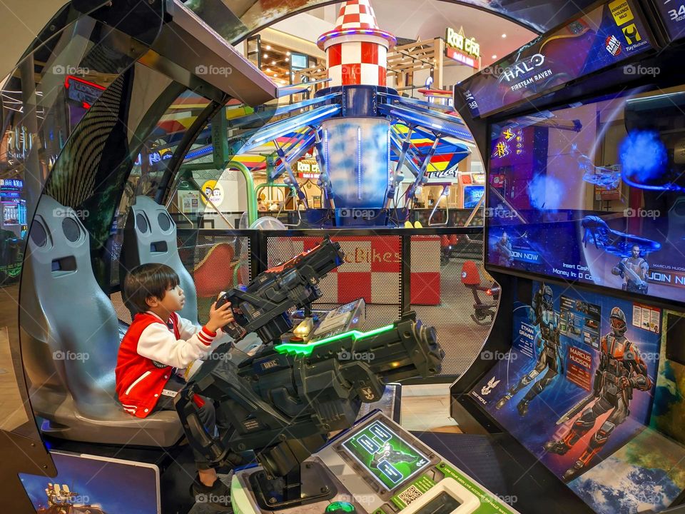 A cute Asian boy is playing video games in the middle of a mall in Tangerang, Banten, Indonesia.