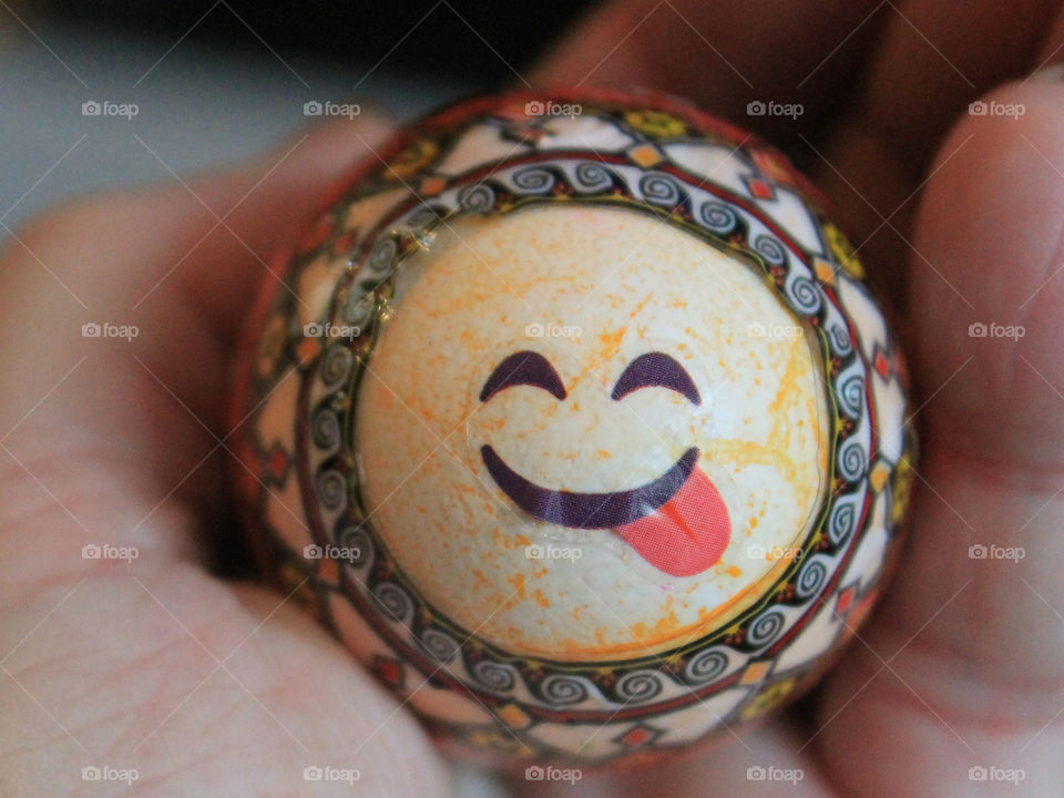 Closeup of a hand held decorated Easter egg. The egg is orange crackle dyed and has a Ukrainian sticker and a smiley face sticker with the tongue sticking out. Handmade by my daughters and niece. 