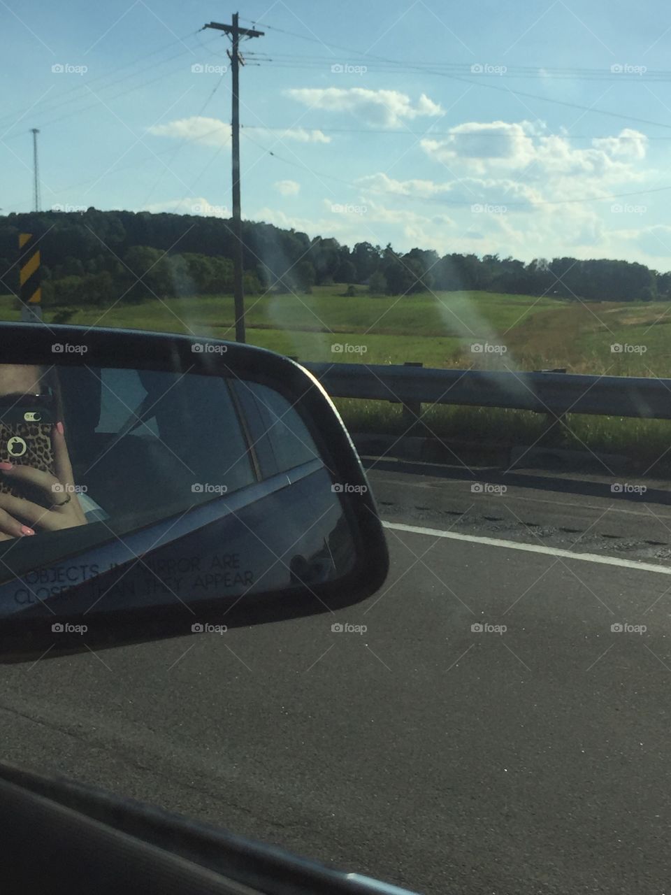 Woman taking photograph with mobile phone in a car side mirror
