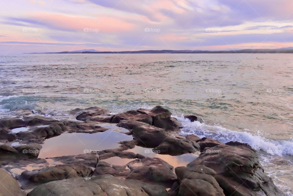 Pink sunset reflects on rock pools on the Australian coastline.