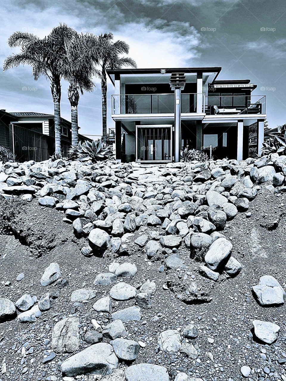 A modern home set just off the sea shore. Black and white. The rocks make for a unique back yard look.