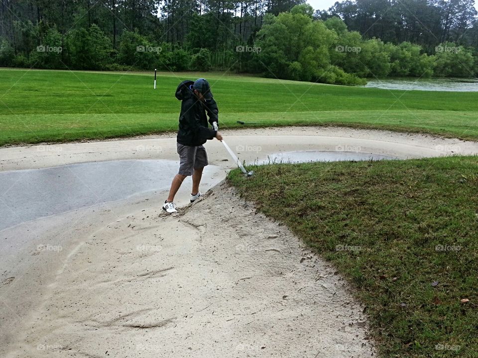 golf shot from a bad lie in the sand bunker with water puddles